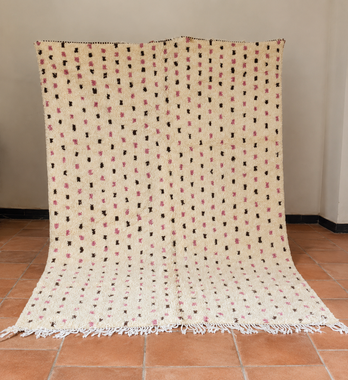 A cream-colored Moroccan-style woven throw blanket with pink and brown geometric patterns.