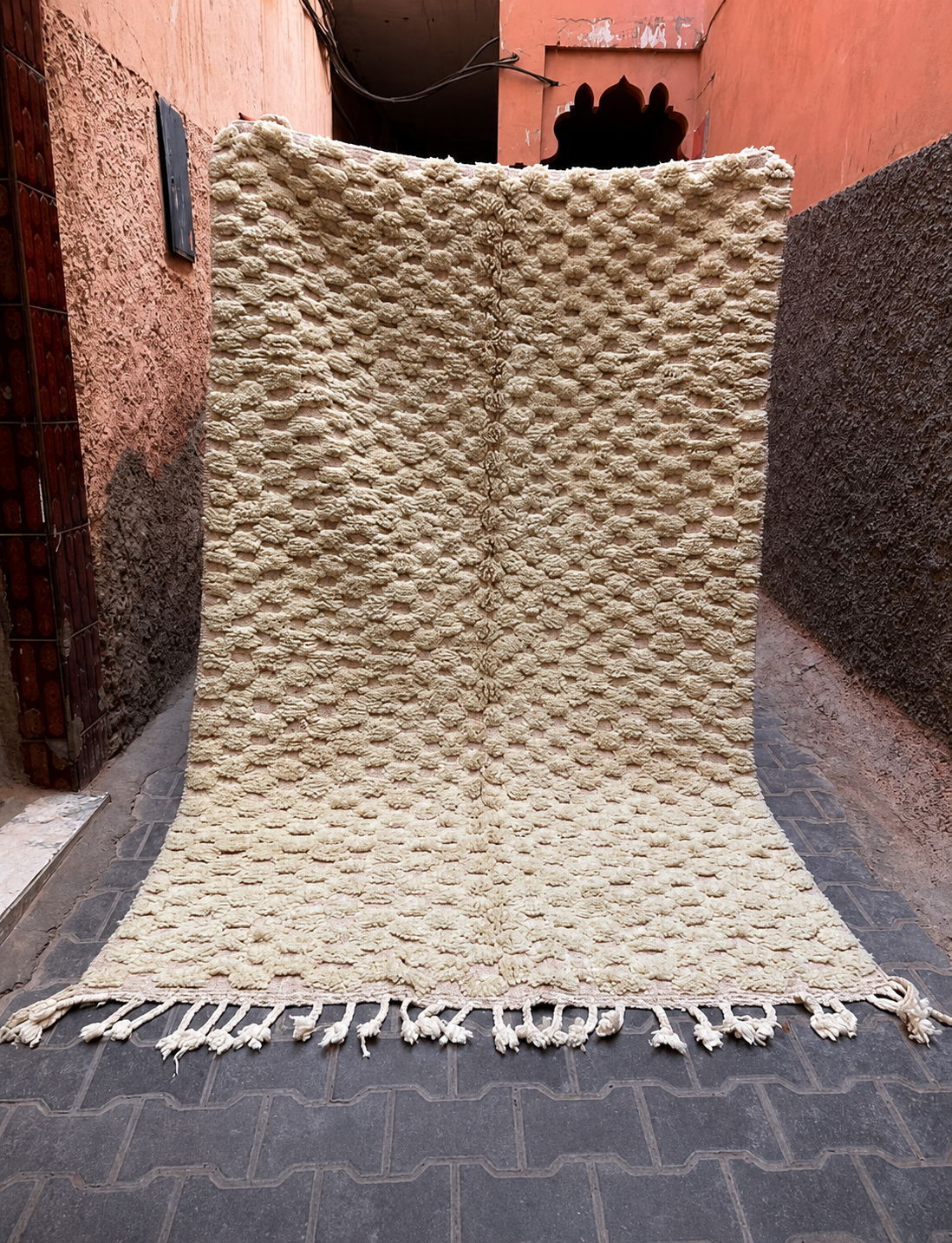A large cream and sage green coloured textured rug with fringe tassels.